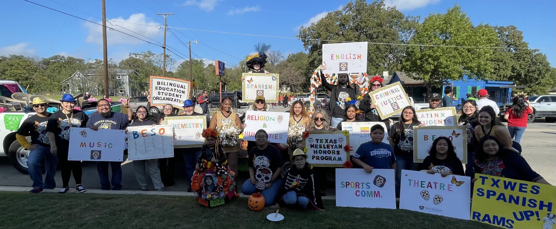 Students, faculty and staff posing at the 2023 Dia de los Muertos parade holding signs representing their student organizations