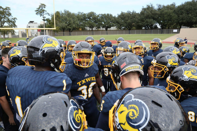 Photo of TXWES football team in a huddle before their homecoming weekend game.