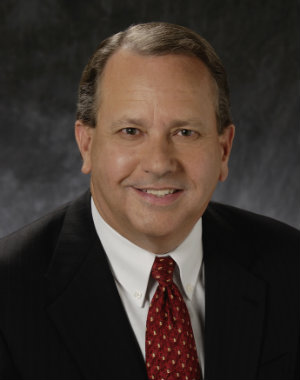 Close up photo of a man in a black suit and red tie