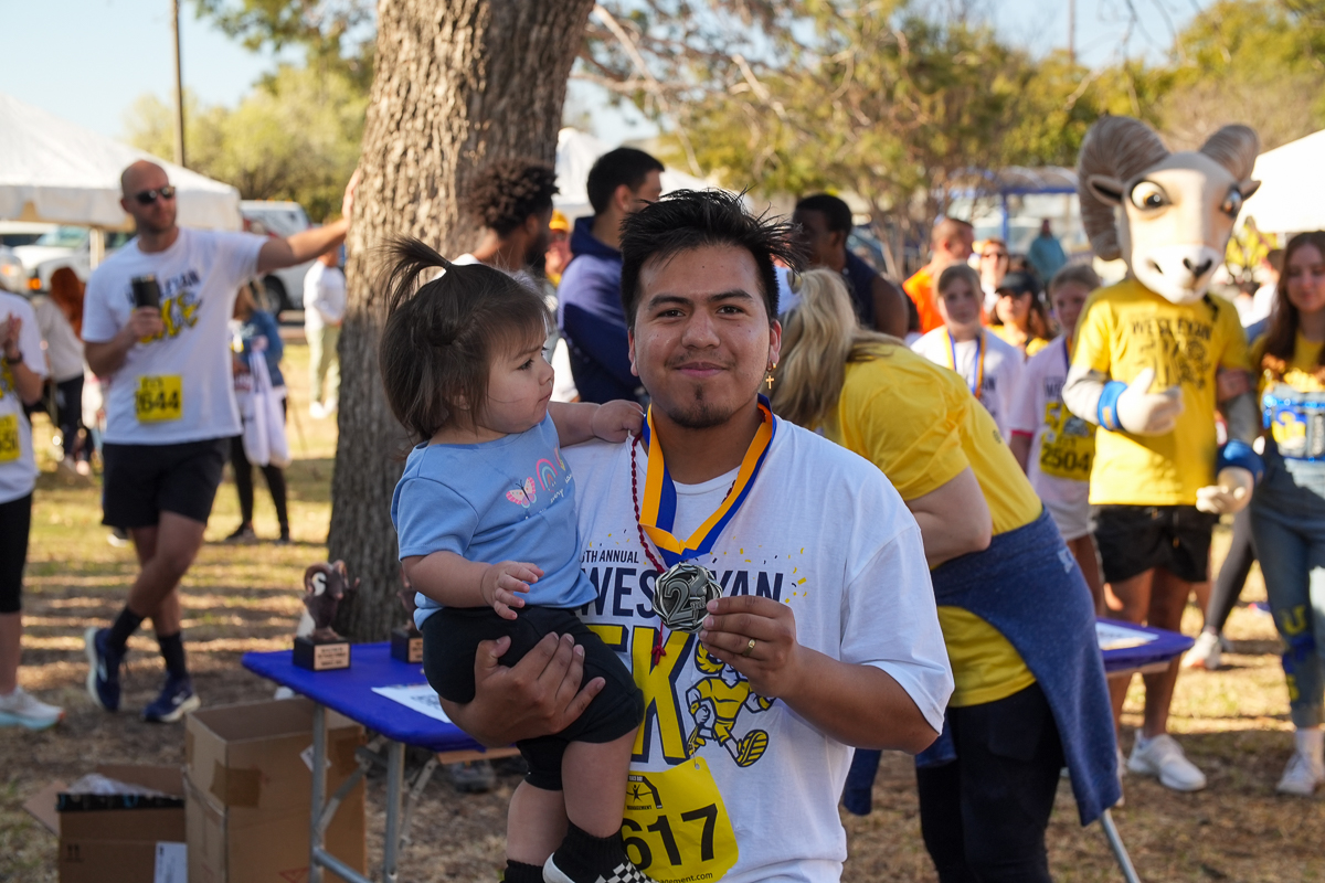 Man smiling while holding child and medal from 5k