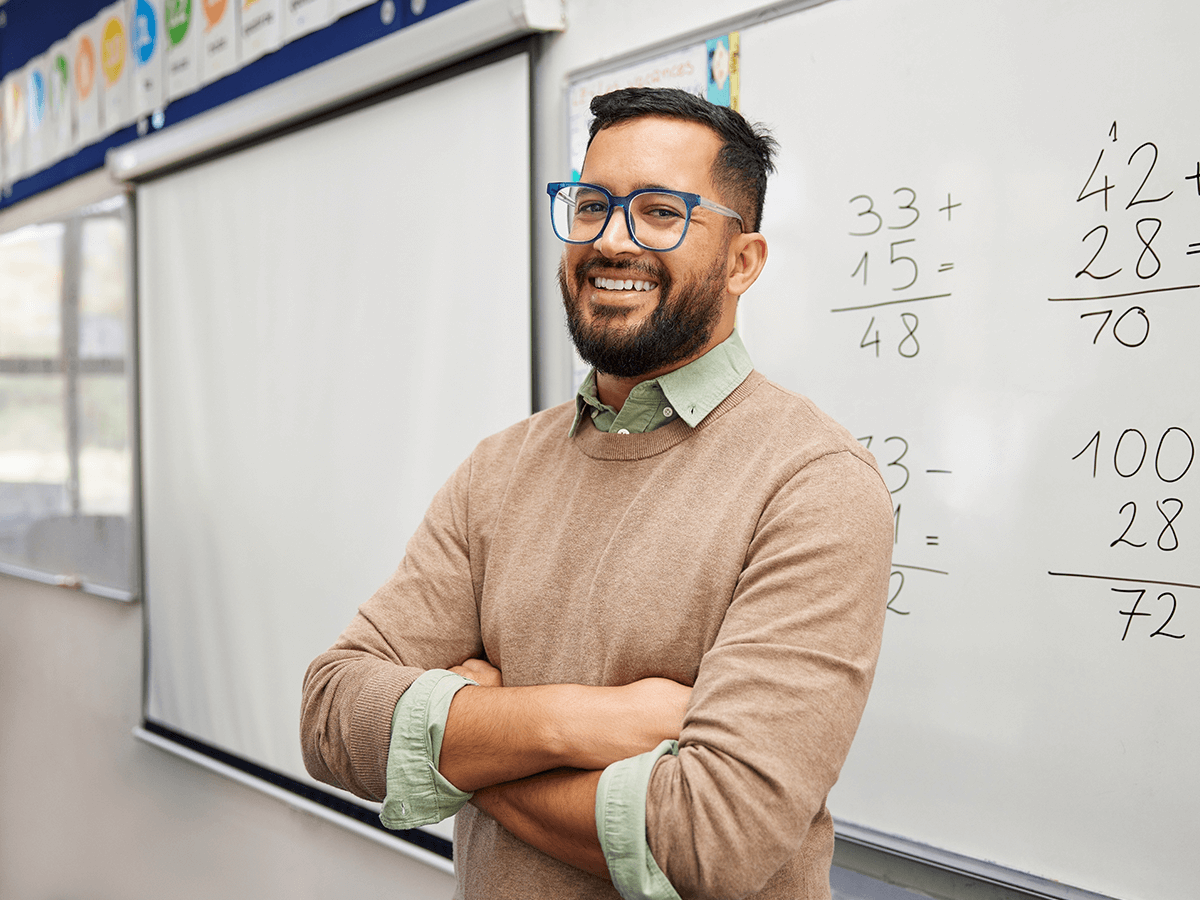 A man leaning against a white board smiling at the class