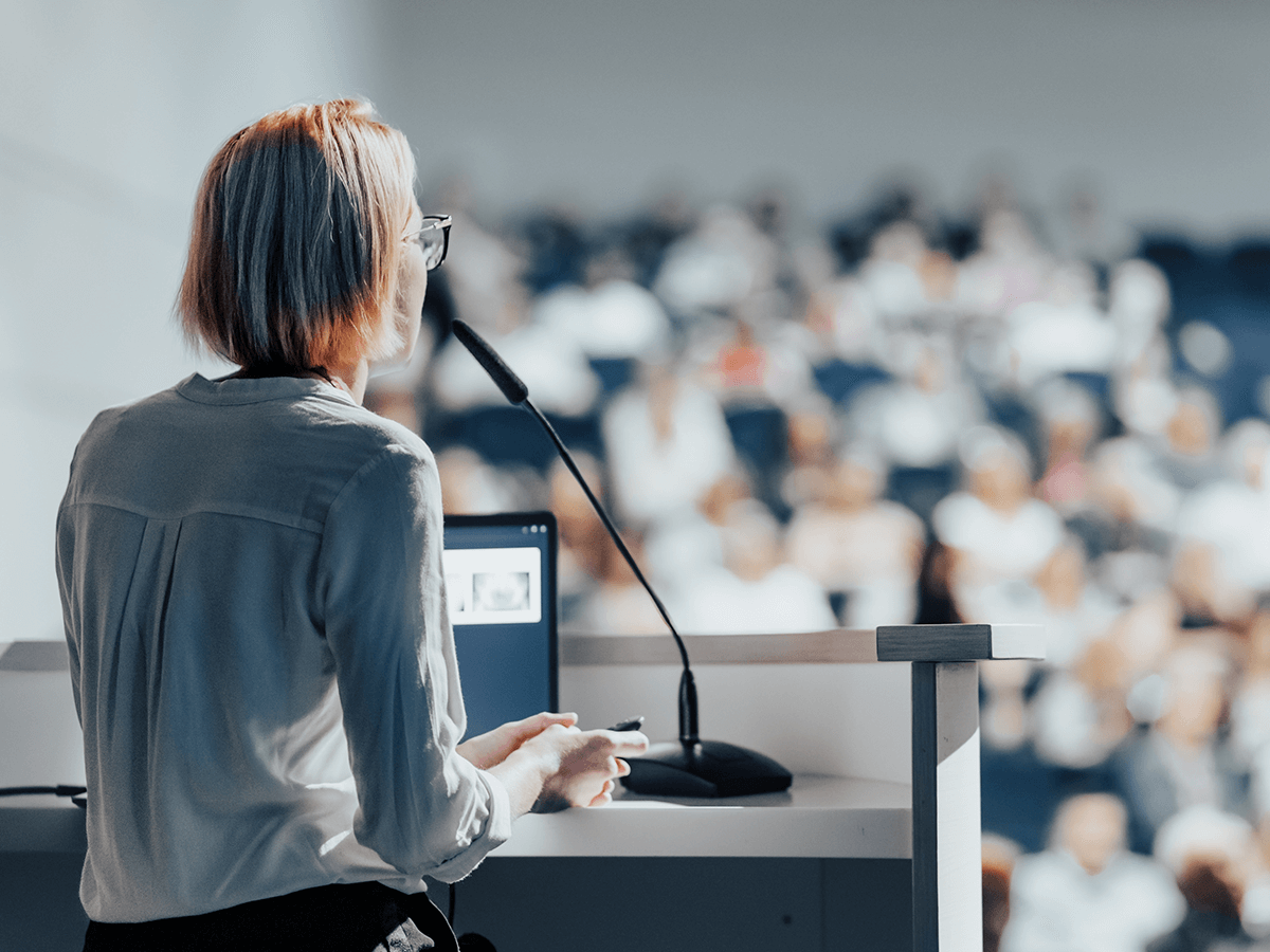 A woman at a Podium giving a lecture to a class