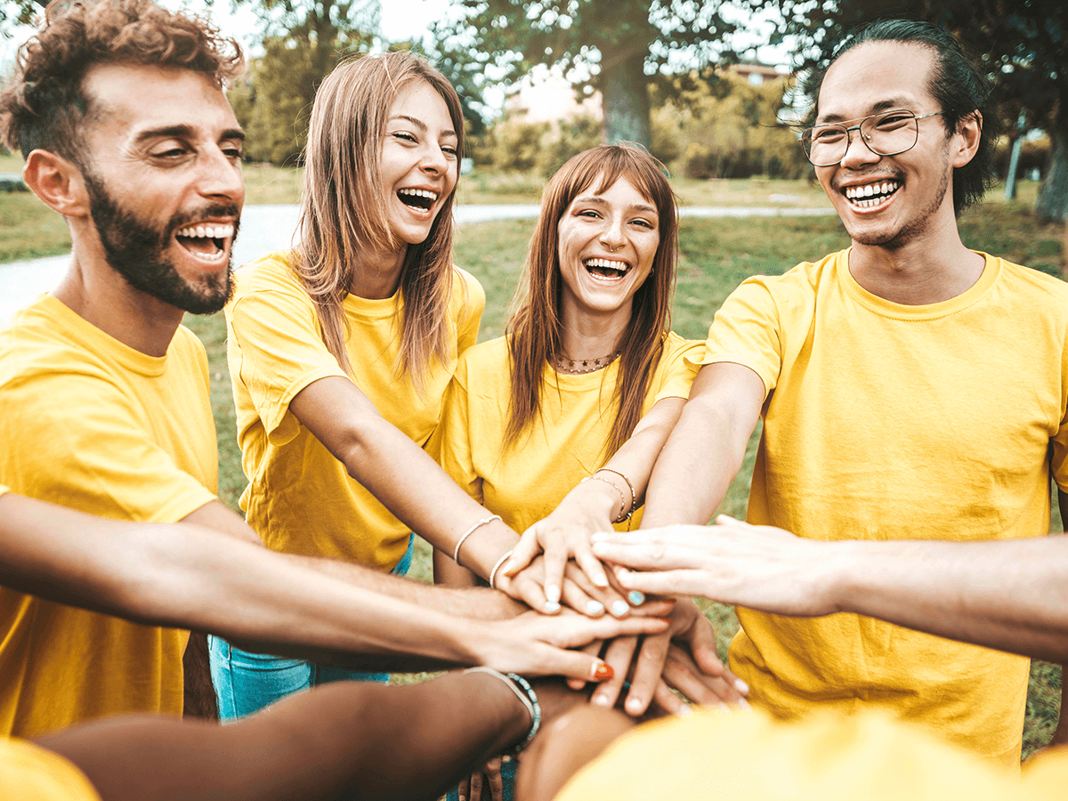 College kids in yellow shirts with all there hands in the middle ready to cheer