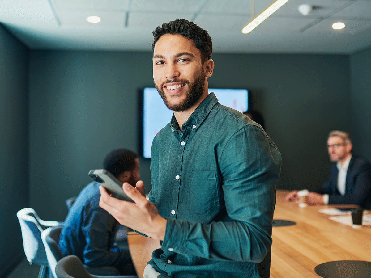 Male business administration major sitting in a boardroom, holding a smartphone.