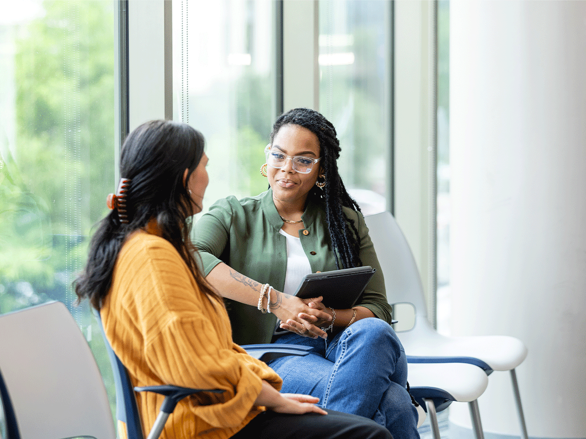 A female student speaking to a female campus counselor in a university hall near windows.