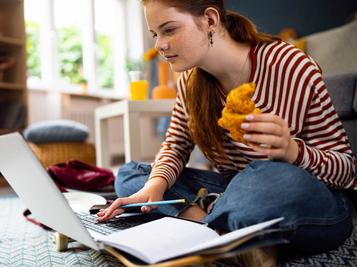 Female student eating a croissant while working on her laptop.