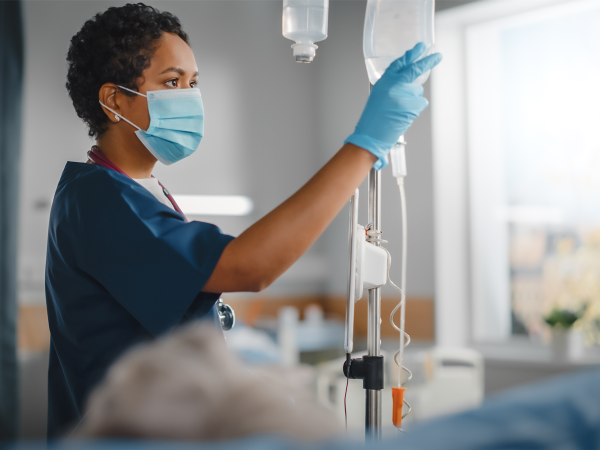 Female nurse anesthetist checking an IV bag, wearing gloves and a mask.