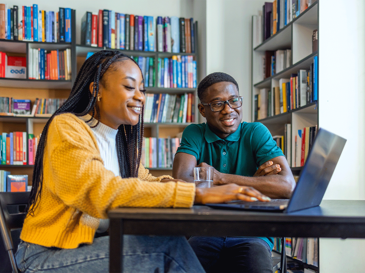 Two students looking at a shared laptop in a library.