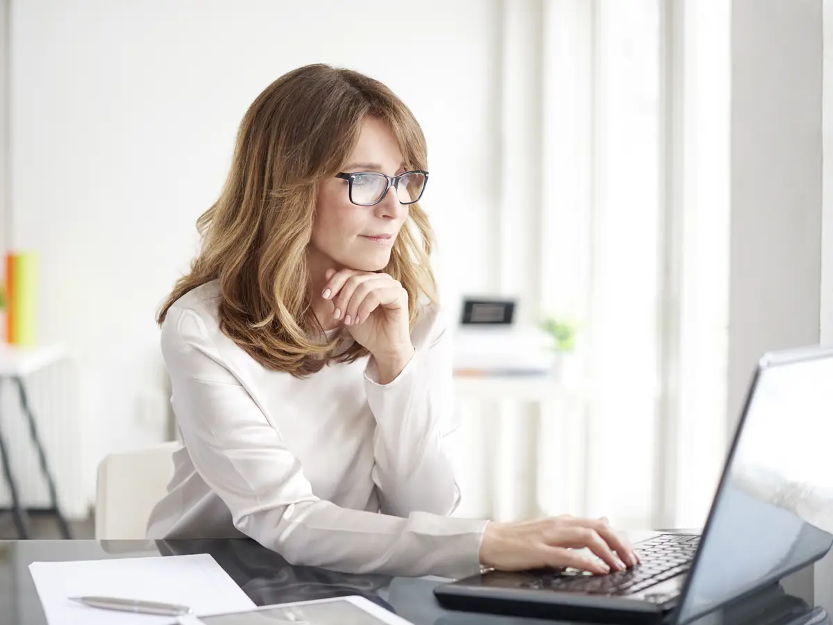 Business woman in white sweater looking at laptop presumably at home
