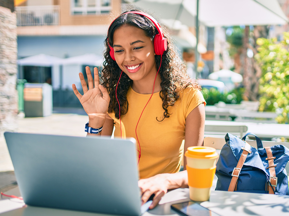 Female Student Outside Happily Waving to Online Classmates