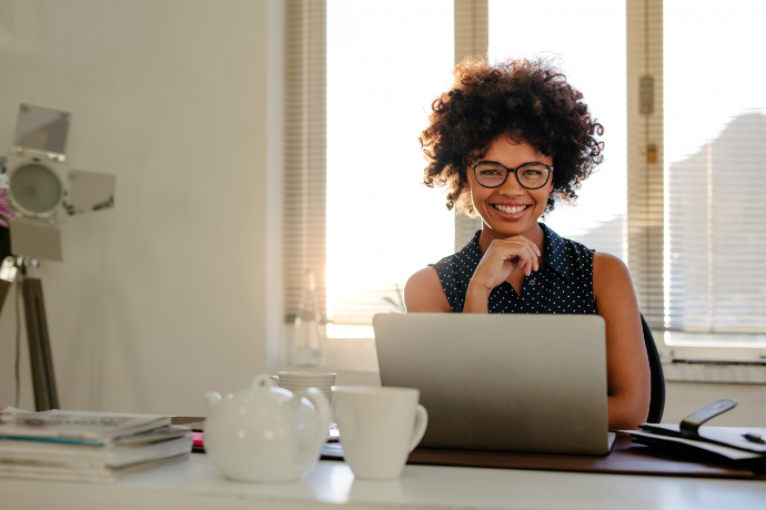 Woman sits behind laptop, smiling
