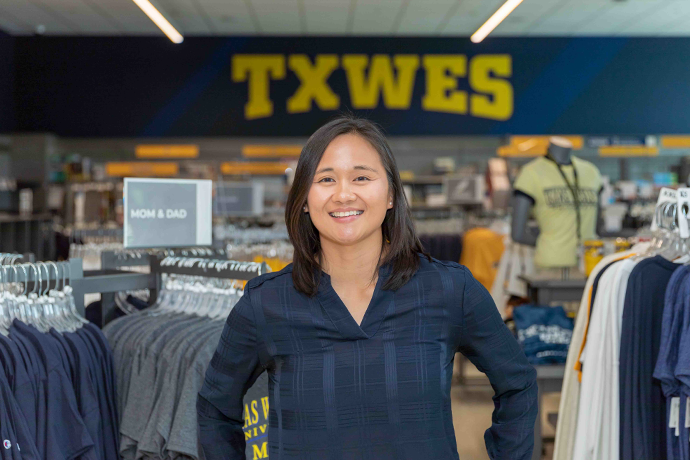TXWES Senior brand manager and graphic designer Paula Tran standing in front of the texas wesleyan bookstore