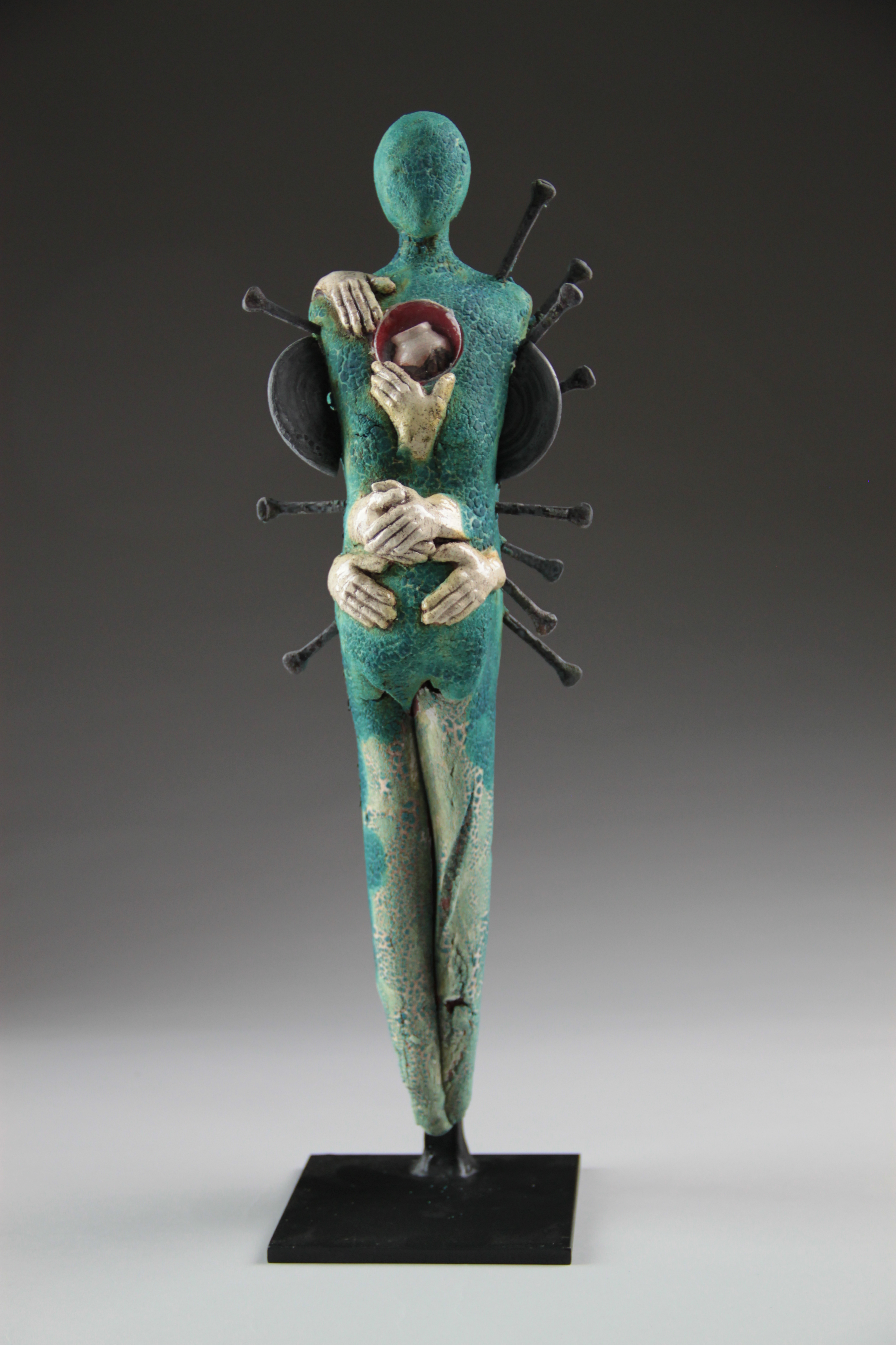 A back of a single figure with pairs of hands seemingly wrapped around the figure.  It has spikes invading the sides of the gender-less form. It is three dimensional and mixed media. 
