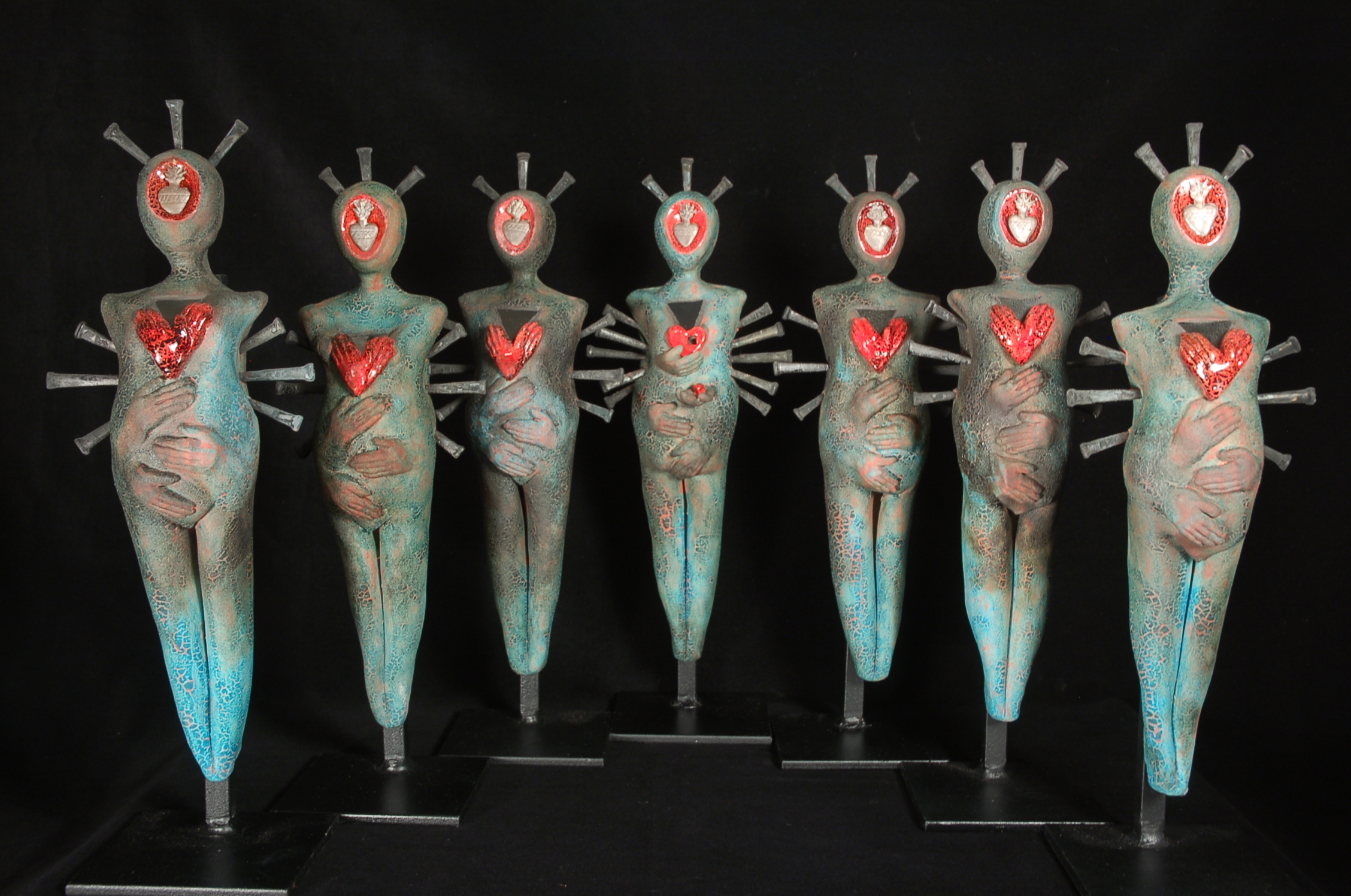 Seven female sculptural ceramic figures lined up. Hands are caressing the belly and torso areas. 