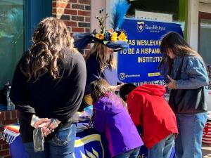 Children and their parents pick up Texas Wesleyan merchandise at. table at the Dia de los Muertos festival in Fort Worth