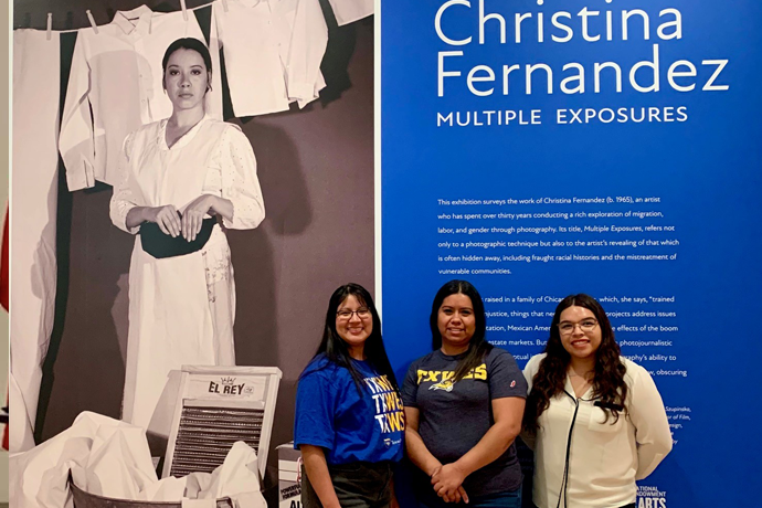 A group of female Texas Wesleyan students standing in front of a large exhibit entitled 