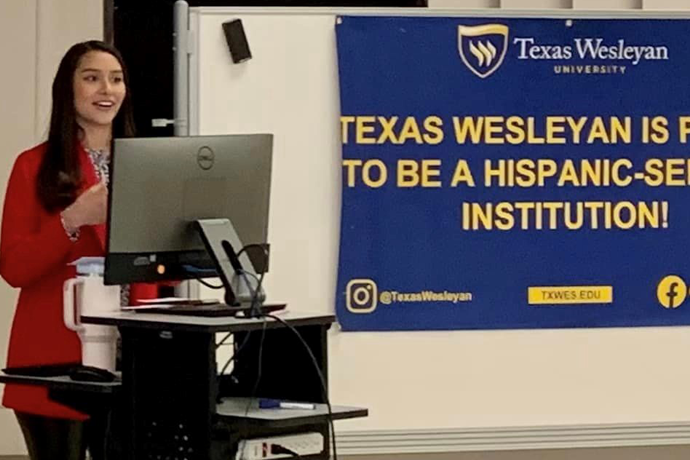 A student presenting at a podium in front of a large blue banner that says 