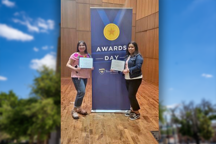 Two Spanish Major students holding certificates standing in front of a large banner that says Awards Day