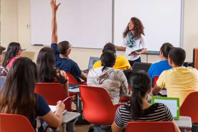 A teacher in a classroom with a student raising their hand