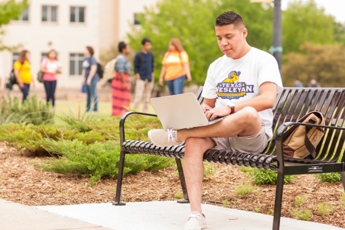 A Texas Wesleyan student sitting on a bench working on his laptop