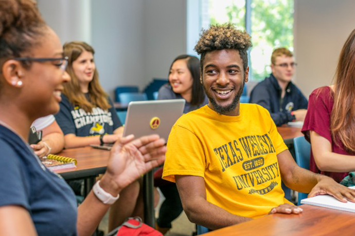 A student in a Texas Wesleyan shirt talking to a classmate in a classroom