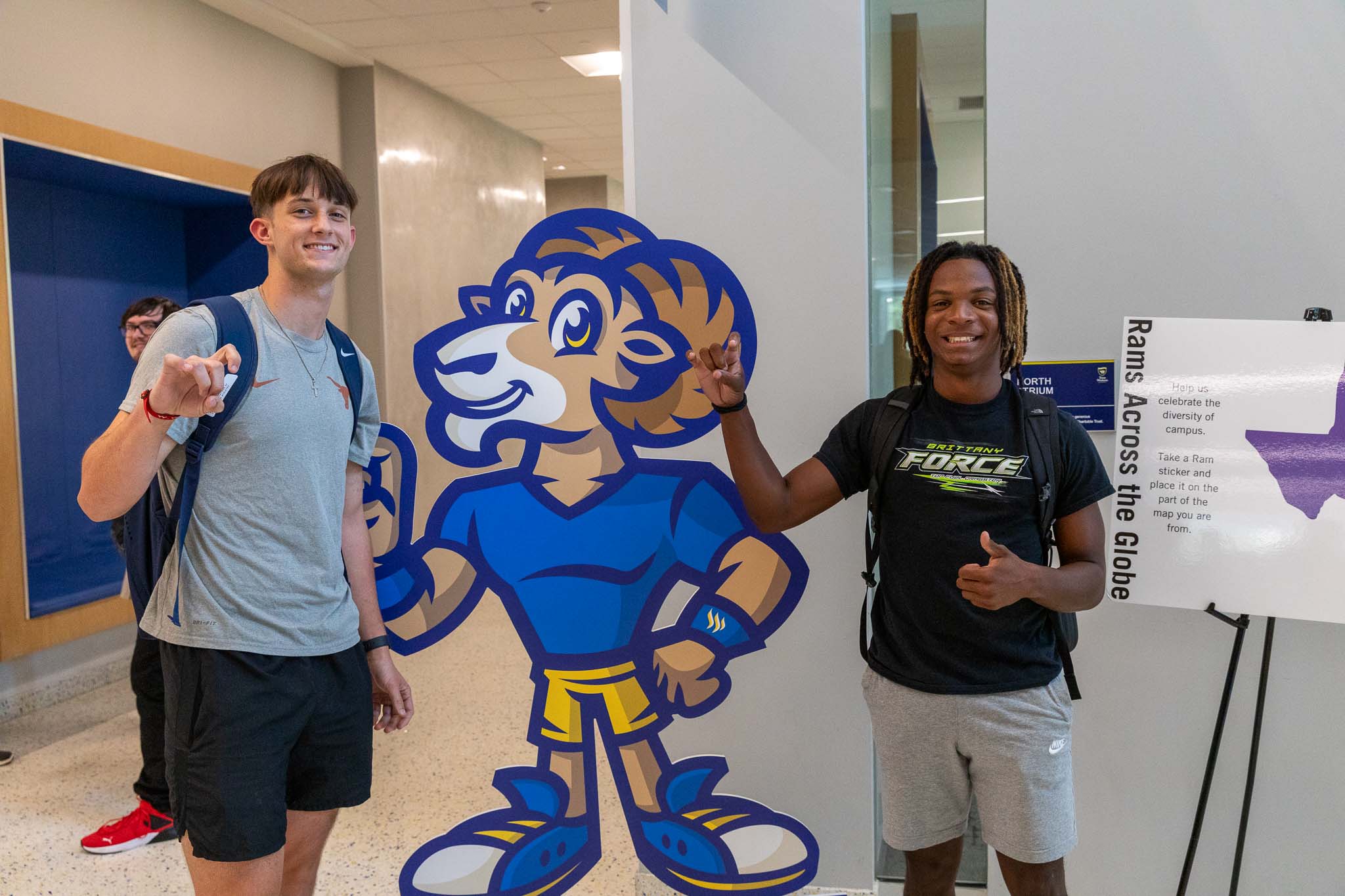 Two male students do the Rams Up sign with a cutout Willie the Ram